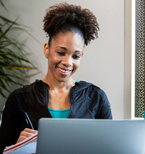 Aspiring ACE Specialist studying online with laptop and notebook, excited to grow her health and fitness career